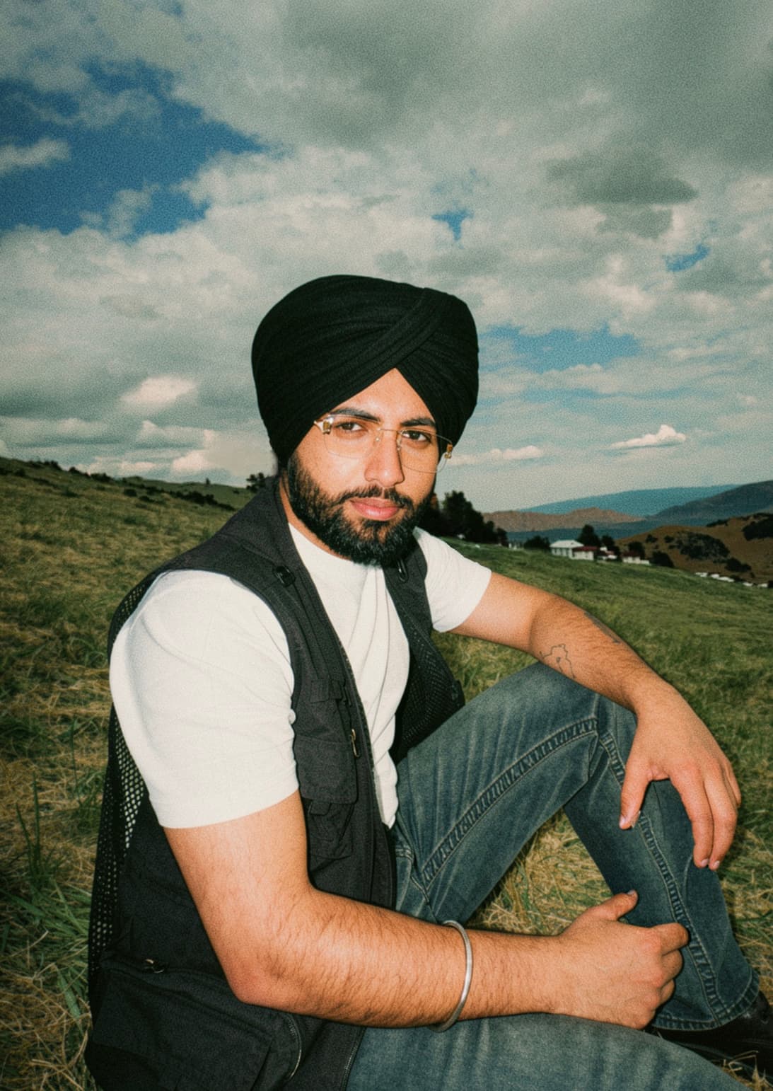 Kirat Sandhu seated on a hillside meadow under an open sky